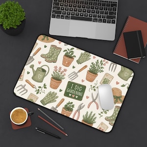 May include: A rectangular desk mat featuring a cream-colored background with a repeating pattern of gardening tools, potted plants, green boots, straw hats, and seed packets. A central green sign displays the text I DIG GARDENING with small hearts.