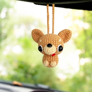 Può includere: Un ornamento all'uncinetto color marrone chiaro a forma di chihuahua con grandi occhi neri in plastica, un muso più chiaro e una piccola lingua rossa che sporge. La figura ha orecchie a punta ed è appesa a un cappio di filo coordinato.