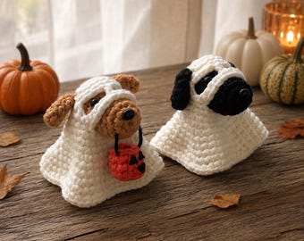 Puede incluir: Dos figuras de perro tejidas a ganchillo disfrazadas de fantasmas con hilo blanco. Un perro es marrón con un pequeño cubo de calabaza naranja, y el otro es blanco y negro. Ambos tienen ojos y narices oscuras, cubiertos por disfraces de fantasma.