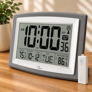 May include: A digital wall clock with a gray and white frame featuring a large LCD screen displaying the time 10:00, the date 10-12, the day TUE, indoor temperature 75.2 degrees Fahrenheit, and outdoor temperature 86.5 degrees Fahrenheit.