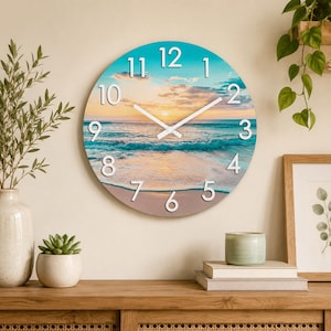 May include: A round wall clock featuring a printed image of a beach at sunset with turquoise ocean waves, sandy shores, and a golden sky. The clock face displays large, white, three-dimensional Arabic numerals from 1 to 12 and two white hands.