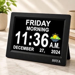 May include: A black digital clock with a rectangular frame displaying the text FRIDAY MORNING, 11:36 A.M., and DECEMBER 27, 2024. The screen features a yellow sun icon above green hills and blue water, with the brand name SSYA printed in white.