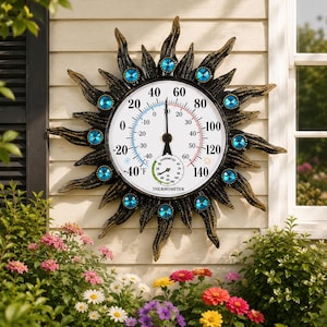 May include: A round outdoor thermometer and hygrometer featuring a sunburst frame in a dark bronze finish with gold highlights. The center dial displays temperatures from -40 to 140 degrees Fahrenheit and includes a small circular humidity gauge.