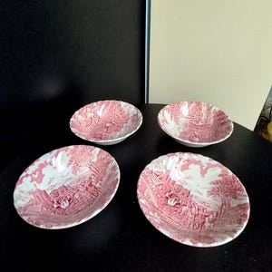 Può includere: Un set di quattro ciotole rotonde in ceramica con un motivo transferware rosa e bianco. Il design raffigura una dettagliata scena pastorale con una carrozza trainata da cavalli, alberi e strutture architettoniche in rosa scuro su base bianca.