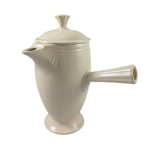 May include: A cream-colored ceramic coffee pot featuring a tall, tapered body, a side-mounted handle, a short spout with ribbed detailing, and a matching lid with a fluted knob. The vessel stands on a circular pedestal base with a smooth finish.
