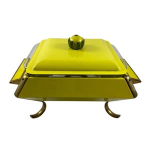 Puede incluir: Una fuente de servir amarilla vintage con tapa a juego y pomo decorativo. La fuente tiene detalles dorados y patas curvas. La tapa tiene una sección de vidrio transparente. Una pieza elegante para servir comida.