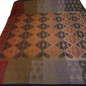 May include: A large, rectangular blanket with a geometric pattern in shades of orange, brown, red, and purple. The design features diamond and stylized floral motifs, creating a patchwork effect. The blanket has a dark border.