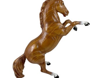 May include: A brown horse figurine rearing up on its hind legs. The horse has a glossy finish with a wood grain pattern. The hooves are black and white, and the mane and tail are detailed.