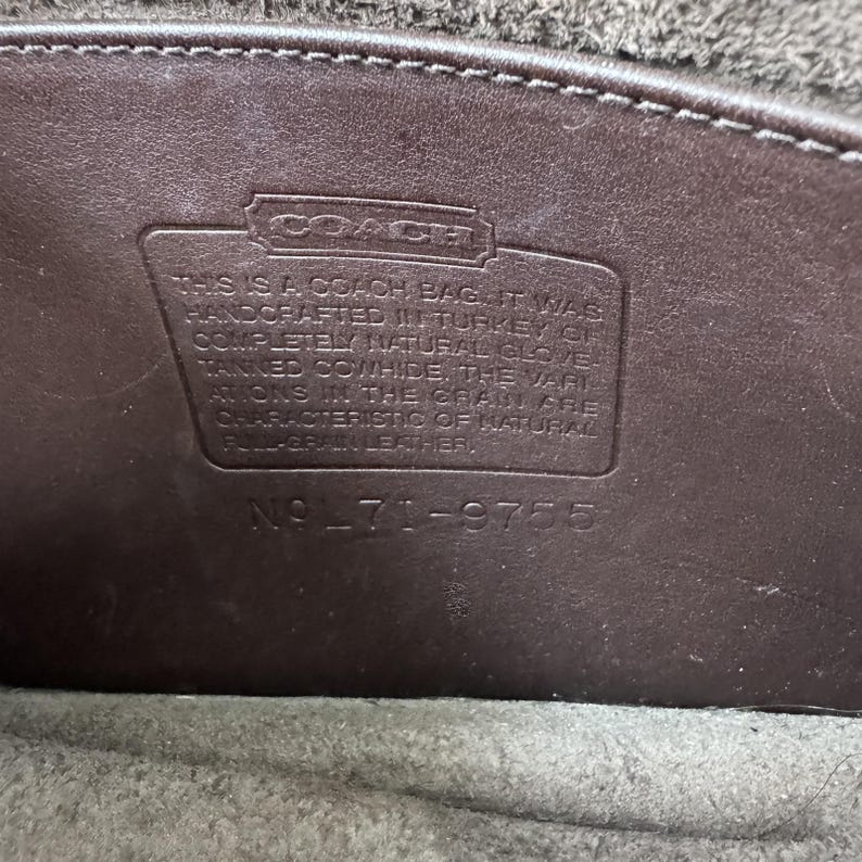K&ouml;nnte beinhalten: Ein dunkelbrauner Lederaufn&auml;her im Inneren einer Coach-Tasche mit dem gepr&auml;gten Text: THIS IS A COACH BAG. IT WAS HANDCRAFTED IN TURKEY OF COMPLETELY NATURAL GLOVE-TANNED COWHIDE. THE VARIATIONS IN THE GRAIN ARE CHARACTERISTIC OF NATURAL FULL-GRAIN LEATHER. NO L71-9755.