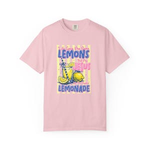 Puede incluir: Una camiseta de manga corta de color rosa claro con un estampado gráfico de un vaso de limonada con rodajas de limón y una pajita a rayas. El texto dice: Life Gave Me Some LEMONS But My JESUS Be Makin LEMONADE, sobre un fondo de rayas amarillas.