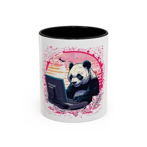 May include: White ceramic coffee mug with a black interior featuring a panda bear using a computer. The panda is black and white with blue eyes, set against a pink and orange background. The mug has a wraparound design.