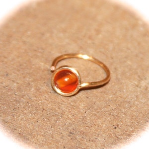 May include: A gold nose ring with a small, round, orange gemstone.