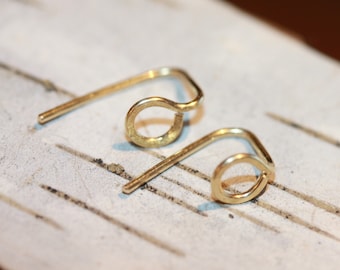 以下が含まれることがあります： シンプルなループデザインの金色のワイヤーイヤリングが2つ。イヤリングは白い表面の上に置かれています。