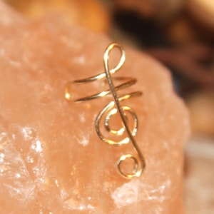 May include: Gold treble clef ear cuff. The cuff is made of wire and is shaped like a treble clef. It is a simple and elegant piece of jewelry.
