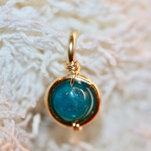May include: A gold wire wrapped pendant featuring a round, blue gemstone with a speckled texture.