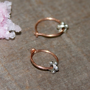 May include: Two small hoop earrings made of copper wire with a silver bead accent. The beads are round and have a textured surface.