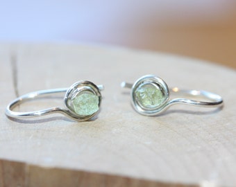 May include: A pair of silver rings, each featuring a light green gemstone set in a wire-wrapped design. The rings are simple and delicate.