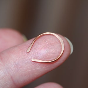 May include: A simple, minimalist gold nose ring. The ring is made of a thin wire and is shaped like a horseshoe.