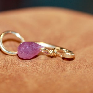 May include: A silver ring with a purple gemstone attached to it. The ring is on a brown surface.
