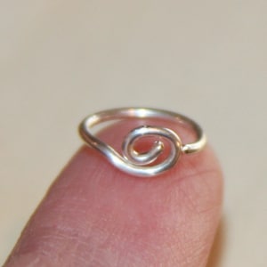May include: A silver ring with a simple, twisted design. The ring is made of wire and has a smooth, polished finish.