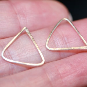 May include: A pair of silver triangle earrings. The earrings are simple and minimalist, with a hammered texture.