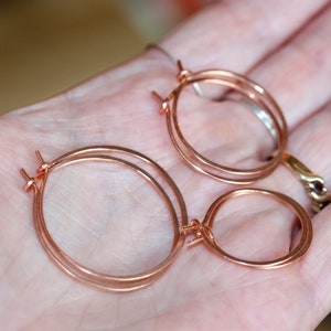 Könnte beinhalten: Ein Paar Ohrringe aus roségoldenen Creolen, wobei ein kleinerer Kreis an den größeren Kreis befestigt ist.