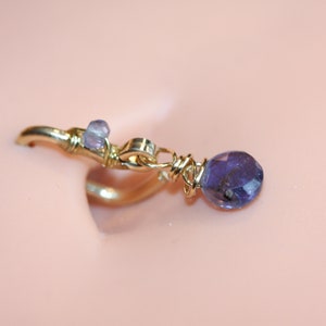 May include: A gold nose ring with a dangling purple gemstone and a smaller purple gemstone on the ring.
