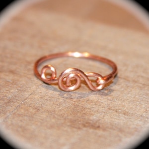 May include: A simple copper wire ring with a swirling design. The ring is made of a single piece of wire that is twisted and shaped to create a unique and delicate look.