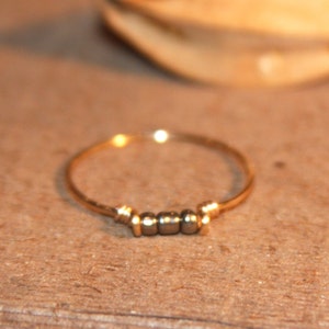 Puede incluir: Un anillo de oro con una fila de pequeñas cuentas de color gris oscuro.
