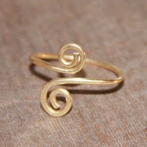 May include: A gold-colored ring with a double spiral design. The ring is made of thin wire and is delicate in appearance.