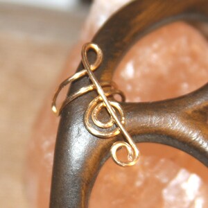 May include: Gold treble clef ear cuff. The cuff is made of wire and is shaped like a treble clef. It is a simple and elegant piece of jewelry.