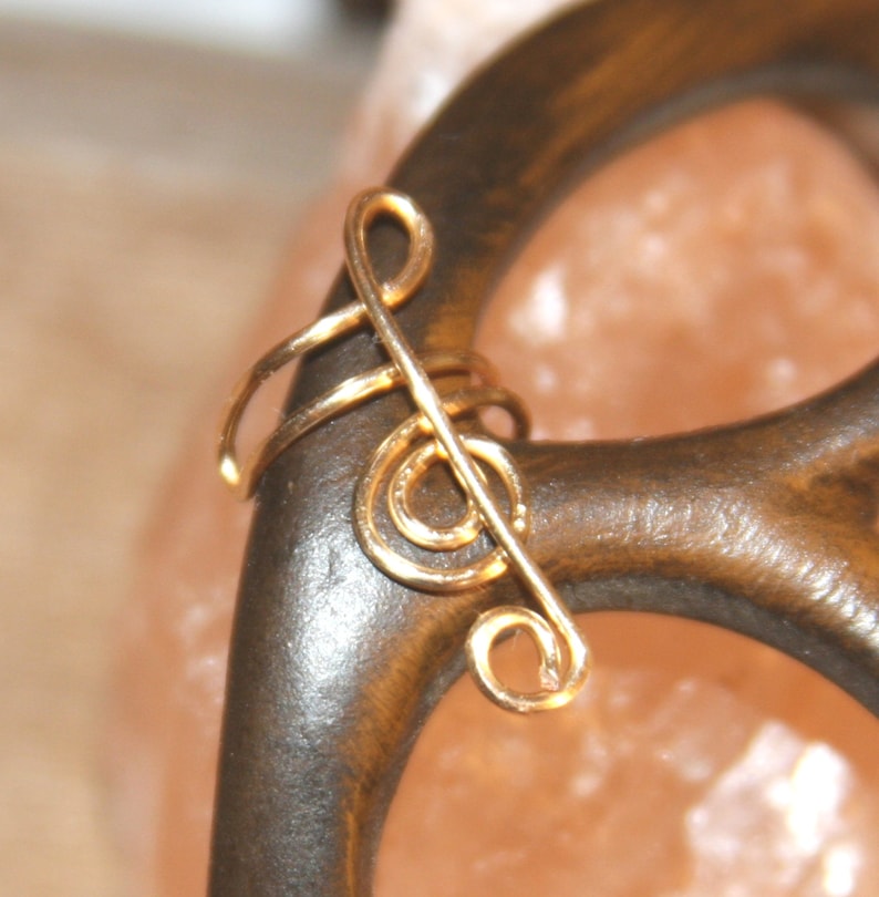 May include: Gold treble clef ear cuff. The cuff is made of wire and is shaped like a treble clef. It is a simple and elegant piece of jewelry.