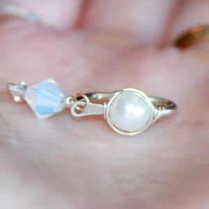 Puede incluir: Un anillo de plata con una perla blanca y un acento de cristal transparente.