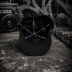 May include: A black baseball cap shown from the interior, featuring a smooth satin-like lining with the text ThirtyOne printed repeatedly on the inner seam tape. The word ThirtyOne is also embroidered in black thread on the underside of the brim.