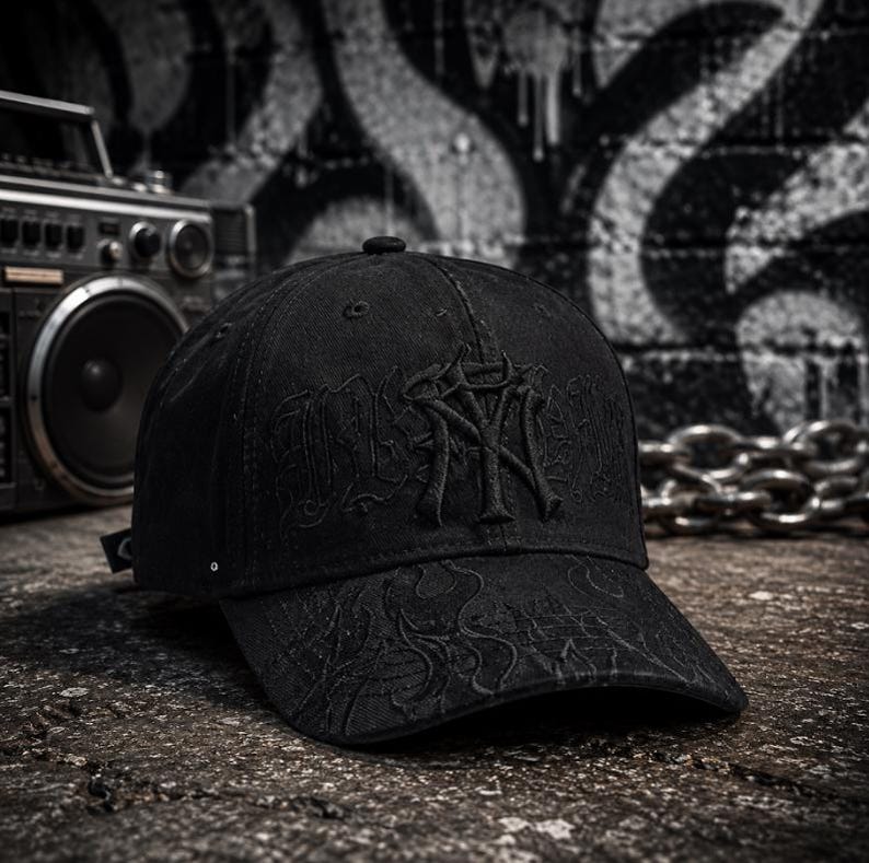 May include: A black baseball cap featuring tonal black embroidery on the front panel and a subtle, dark flame-like pattern stitched across the curved brim. The cap is constructed from a structured fabric with a classic six-panel design and eyelets.