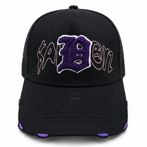 May include: A black trucker hat featuring a mesh back and a structured front panel. The front displays the text "SADBOYZ" in pink stitched lettering with a large, textured purple chenille letter "B" in the center. The brim has distressed edges with purple fabric accents.