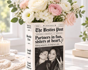 May include: A rectangular ceramic vase shaped like a book, featuring the text The Besties Post, Partners in fun, sisters at heart, and a black and white photo of two people. The vase is filled with a bouquet of white and pink roses and baby's breath.