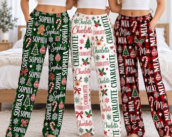May include: Three pairs of pajama pants featuring festive holiday patterns. The green pair displays the name Sophia, the white pair displays Charlotte, and the red and black plaid pair displays Mia, all with Christmas icons like trees and candy canes.