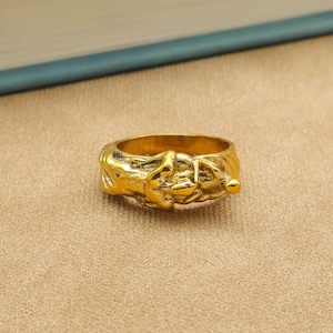 May include: A gold-toned ring featuring a textured, organic, and irregular surface design. The band has a continuous, sculpted appearance with raised, uneven details that wrap around the entire circumference of the circular metal jewellery piece.