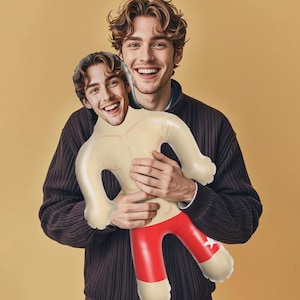 May include: An inflatable doll featuring a custom printed face of a smiling person with brown hair. The doll has a light skin tone, a muscular torso design, and bright red shorts with a white star detail on the left leg. The figure is shaped like a cartoon character with rounded limbs and a smooth, glossy surface finish.