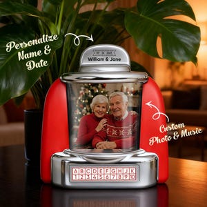 Op de afbeelding: Een jukebox-vormige fotolijst met een rode en zilveren afwerking. De bovenkant bevat de tekst 09-24-2025 en William & Jane. Het midden toont een foto van een ouder echtpaar. De basis bevat een raster met de letters A-K en de cijfers 1-10.