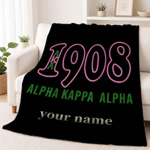 Peut inclure: Une couverture polaire noire avec le nombre 1908 en contour rose et les lettres vertes AKA à l'intérieur du chiffre 1. En dessous, le texte ALPHA KAPPA ALPHA apparaît en vert, suivi du texte de remplacement your name en blanc.