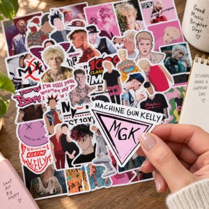 Pode incluir: Uma coleção de autocolantes do Machine Gun Kelly com várias ilustrações, fotografias e designs de texto. Um autocolante triangular em primeiro plano apresenta o texto MACHINE GUN KELLY e MGK em tinta preta sobre um fundo rosa claro.