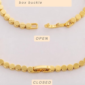 May include: A gold-toned chain bracelet composed of small, flat, circular links. The image displays two views: one with the box buckle in an open position labeled "OPEN" and one with the buckle in a closed position labeled "CLOSED". Text reads "Detailed display of the box buckle".