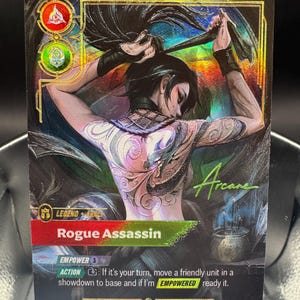 May include: A holographic trading card titled Rogue Assassin featuring a character with a detailed back tattoo, dark hair, and black wristbands. The card displays game text, icons, and the word Arcane in green script against a dark, mystical background.