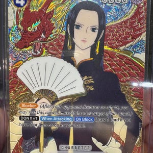 Può includere: Una carta collezionabile olografica di One Piece raffigurante Boa Hancock che tiene un ventaglio bianco. La carta presenta uno sfondo con drago rosso, un livello di potenza di 5000, un costo di 4 e testo che descrive Blocker, DON!!x1 e il personaggio.