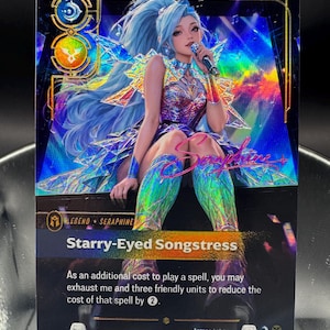 May include: A holographic trading card featuring a blue-haired character named Seraphine holding a microphone. The card displays the text Starry-Eyed Songstress, Arcane Labs, and game rules regarding spell costs, set against a vibrant, prismatic background.