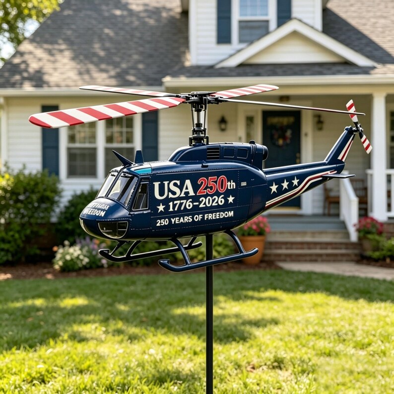 May include: A dark blue metal helicopter garden spinner featuring red and white striped rotor blades. The fuselage displays the text USA 250th 1776-2026 and 250 YEARS OF FREEDOM with white stars. It is mounted on a black pole for outdoor display.
