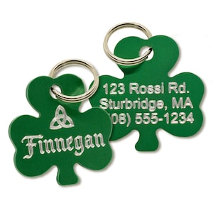 May include: Two green shamrock-shaped pet ID tags with silver text and rings. One tag reads "Finnegan" with a Celtic knot. The other tag has an address and phone number.