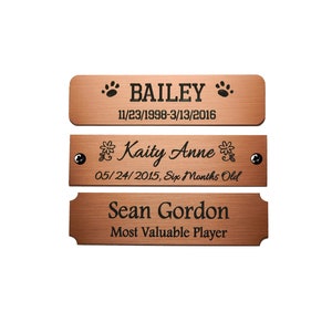 May include: Three bronze-colored rectangular plaques with black engraved text. The top plaque reads "BAILEY" with paw prints and dates. The middle plaque says "Kaity Anne" with floral accents and a date. The bottom plaque says "Sean Gordon, Most Valuable Player."